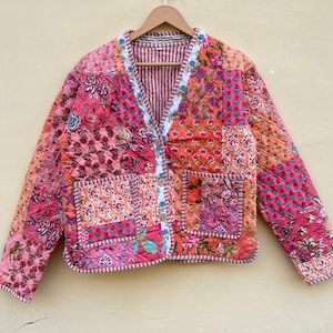 Può includere: Una giacca trapuntata patchwork rosa e arancione con scollo a V e chiusura con bottoni. La giacca ha una stampa floreale ed è realizzata in cotone.