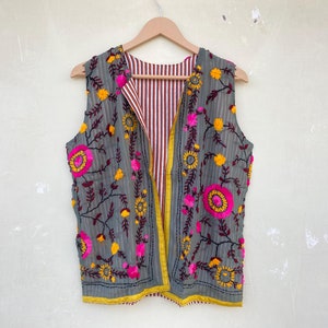 Op de afbeelding: Een grijs vest zonder mouwen met een gestreepte voering. Het vest is geborduurd met roze, gele en donkerrode bloemen.