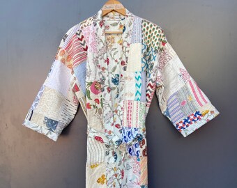 May include: A patchwork robe with a floral and geometric pattern. The robe is made of various fabric squares in shades of white, blue, pink, and orange. It has a tie belt and is hanging on a wooden hanger against a gray background.