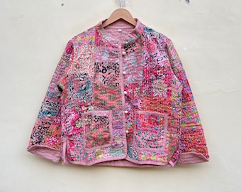 Puede incluir: Chaqueta rosa de patchwork con cuello mandarín y dos bolsillos delanteros. La chaqueta presenta varios estampados florales y geométricos en tonos rosa, rojo y azul. Tiene cierre de botones y está colgada de una percha de madera.
