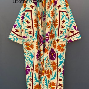 May include: A cream-colored robe with a floral pattern in shades of orange, purple, turquoise, and burgundy. The robe has a long, flowing silhouette and a tie closure at the neck.