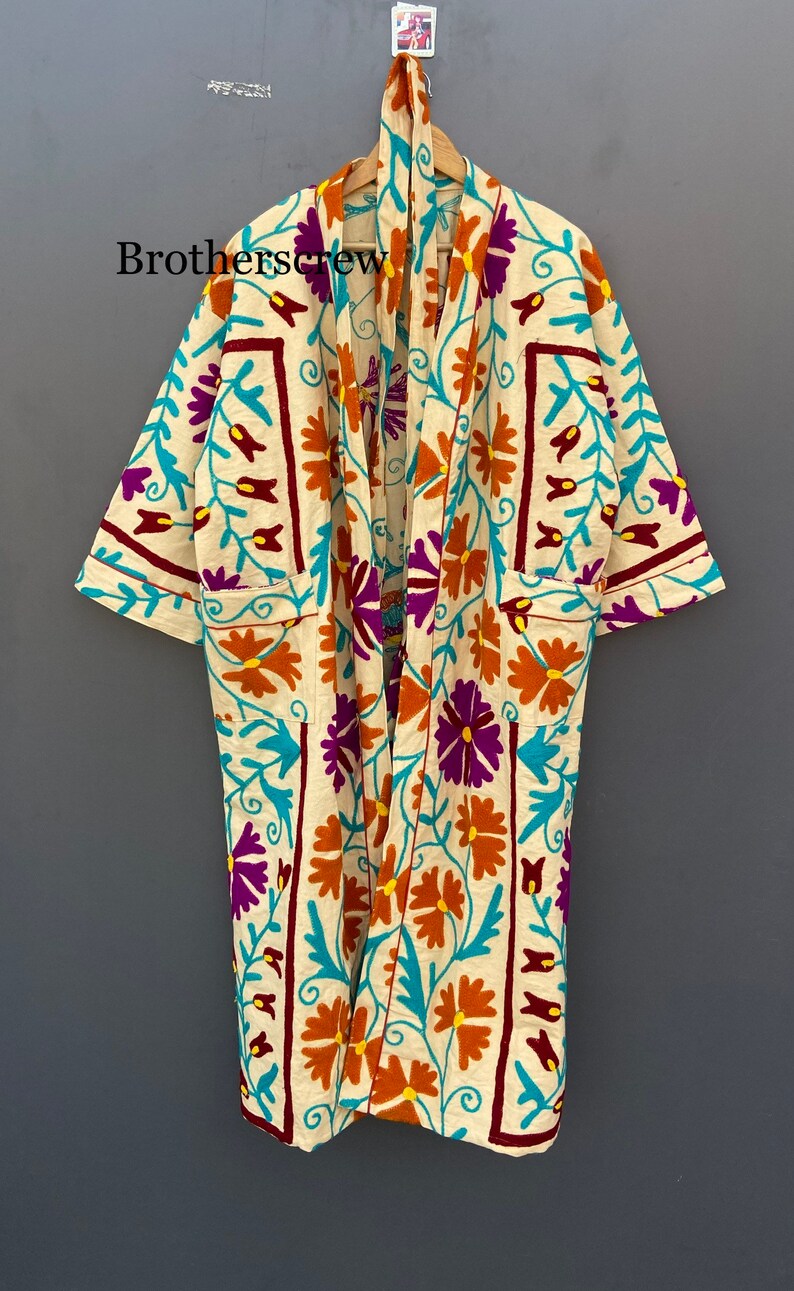 May include: A cream-colored robe with a floral pattern in shades of orange, purple, turquoise, and burgundy. The robe has a long, flowing silhouette and a tie closure at the neck.