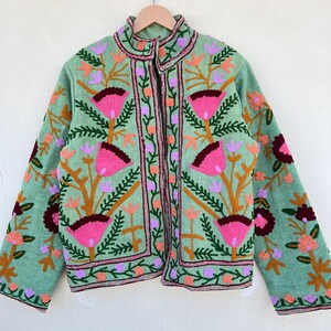 May include: A green embroidered jacket with pink, orange, and purple floral designs. The jacket has a stand-up collar and a zipper closure.