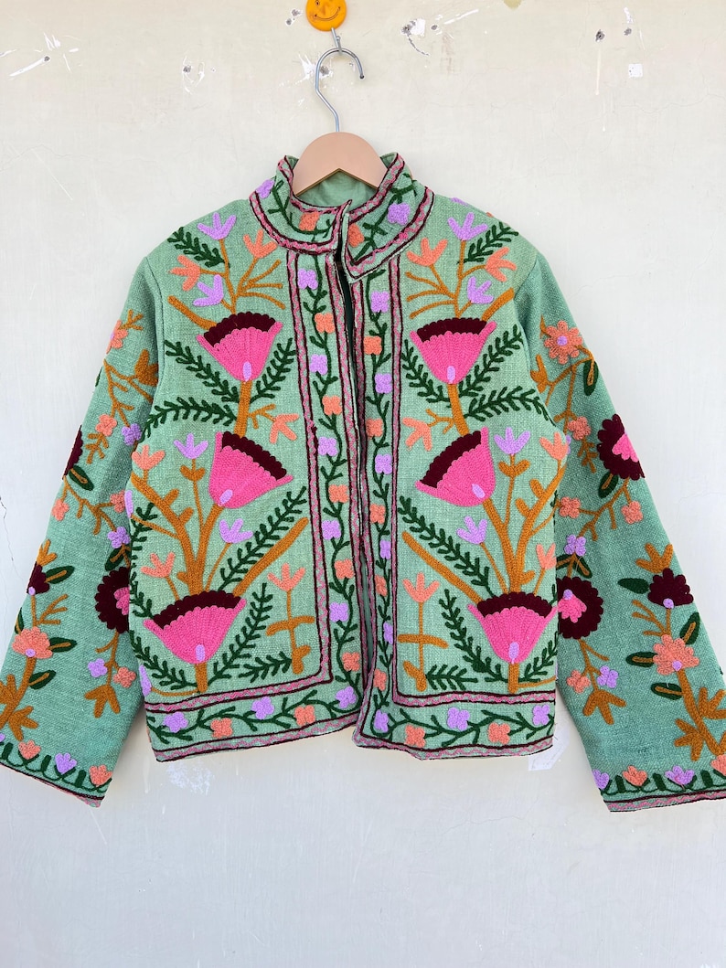 May include: A green embroidered jacket with pink, orange, and purple floral designs. The jacket has a stand-up collar and a zipper closure.