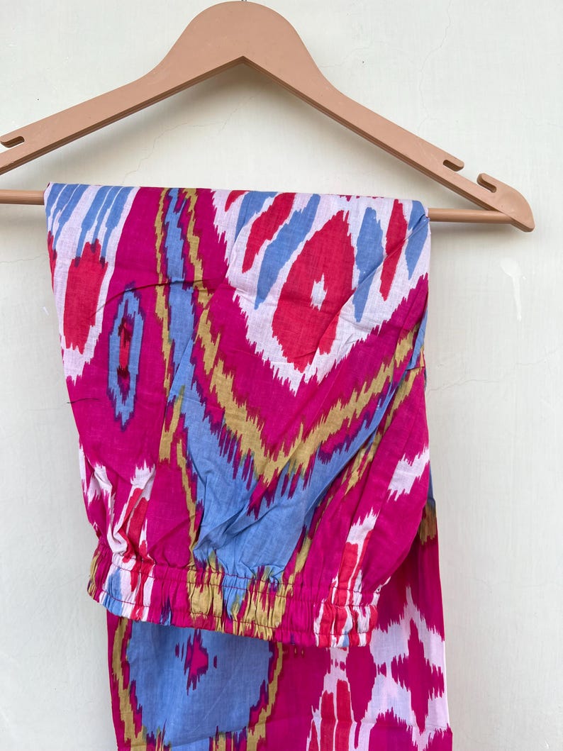 May include: Pink, blue, and gold patterned pants with an elastic waistband. The pants are hanging on a wooden hanger.
