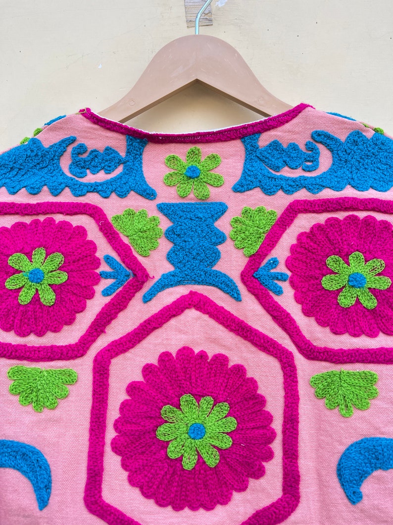 Puede incluir: Una blusa de algod&oacute;n rosa con flores bordadas de colores y patrones geom&eacute;tricos. El bordado est&aacute; hecho en tonos de rosa, verde, azul y blanco.