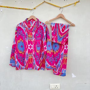 May include: A pink and blue patterned pajama set with long sleeves and pants. The fabric has a geometric design with a white trim.