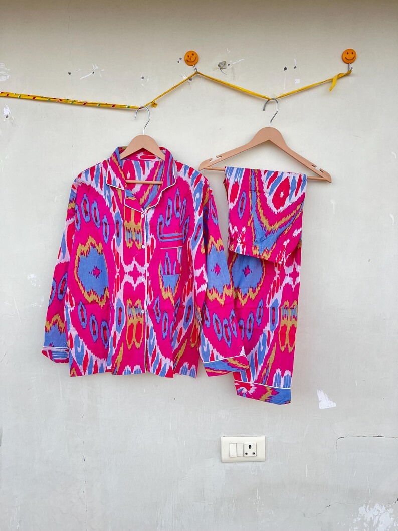 May include: A pink and blue patterned pajama set with long sleeves and pants. The fabric has a geometric design with a white trim.