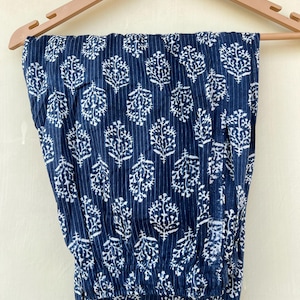 K&ouml;nnte beinhalten: Eine blaue Baumwollhose mit wei&szlig;em Blumenmuster. Die Hose hat einen elastischen Bund und eine lockere Passform.