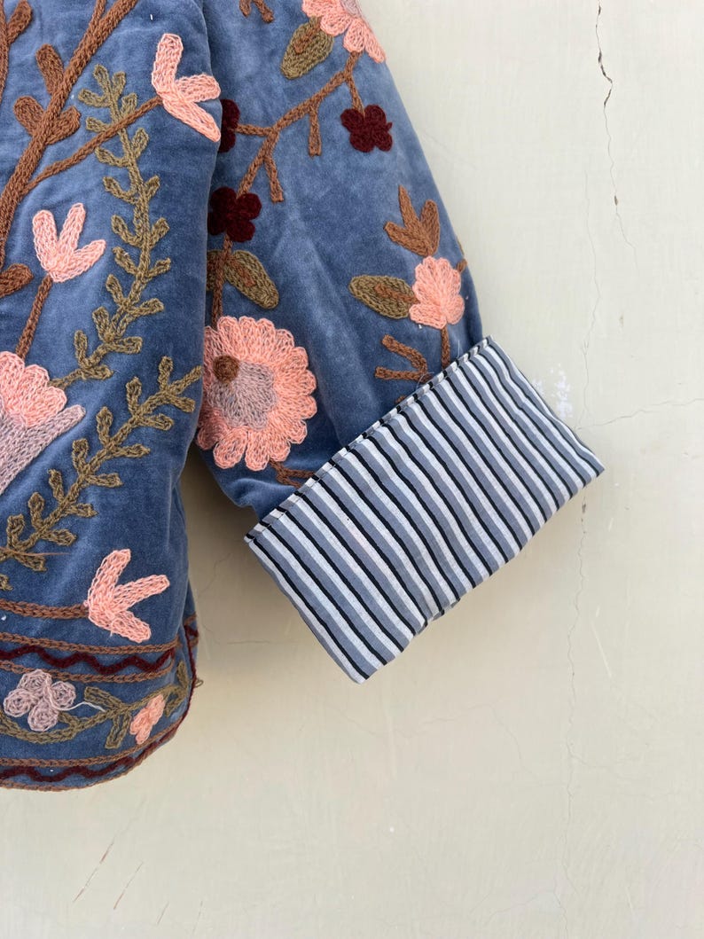 May include: A blue velvet jacket with embroidered floral details. The jacket has a striped cuff detail.