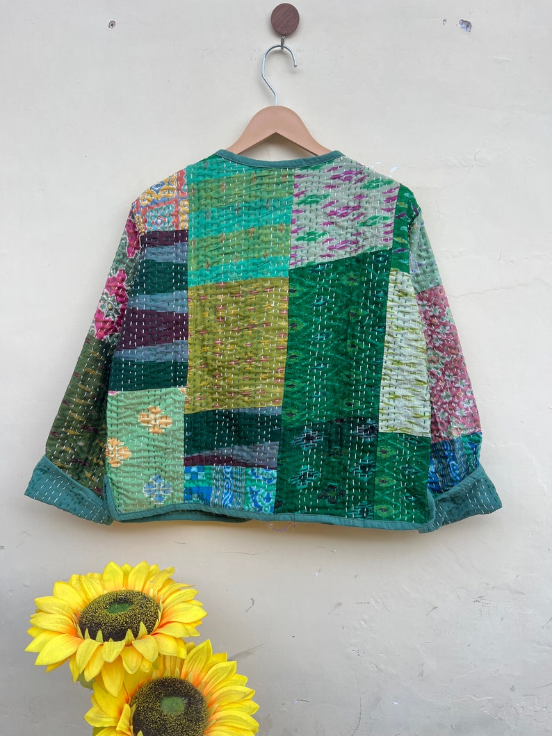 Puede incluir: Una chaqueta acolchada verde con un dise&ntilde;o de patchwork. La chaqueta tiene un cuello redondo y mangas largas. La tela es una mezcla de diferentes patrones y colores, incluyendo verde, azul y rosa.