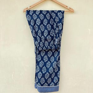 K&ouml;nnte beinhalten: Eine blaue Baumwollhose mit wei&szlig;em Blumenmuster. Die Hose hat einen wei&szlig;en und blauen Streifenbesatz am unteren Rand.