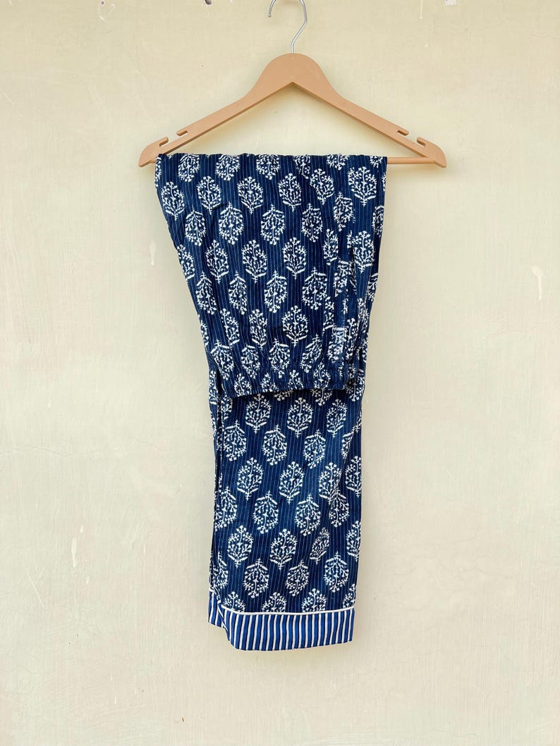 K&ouml;nnte beinhalten: Eine blaue Baumwollhose mit wei&szlig;em Blumenmuster. Die Hose hat einen wei&szlig;en und blauen Streifenbesatz am unteren Rand.