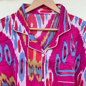 May include: A pink and blue patterned button-up shirt with a white trim. The shirt has a collar and a pocket on the left side.