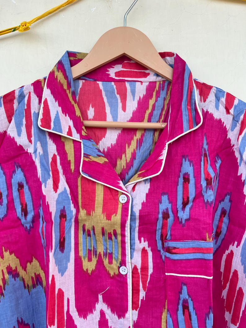 May include: A pink and blue patterned button-up shirt with a white trim. The shirt has a collar and a pocket on the left side.