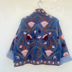 May include: A blue velvet jacket with embroidered floral designs in shades of pink, brown, and burgundy. The jacket has a striped trim on the cuffs.