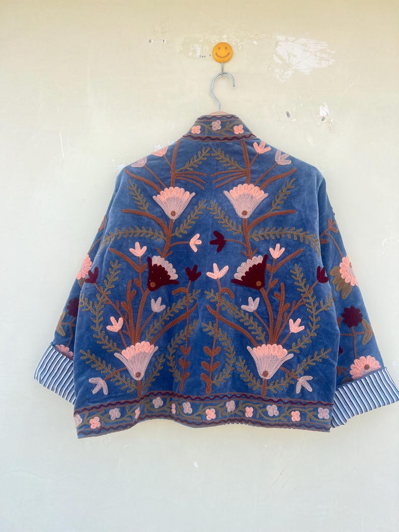 May include: A blue velvet jacket with embroidered floral designs in shades of pink, brown, and burgundy. The jacket has a striped trim on the cuffs.
