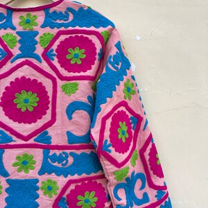 Puede incluir: Una chaqueta rosa con coloridos patrones florales bordados en tonos azules, verdes y rosas.