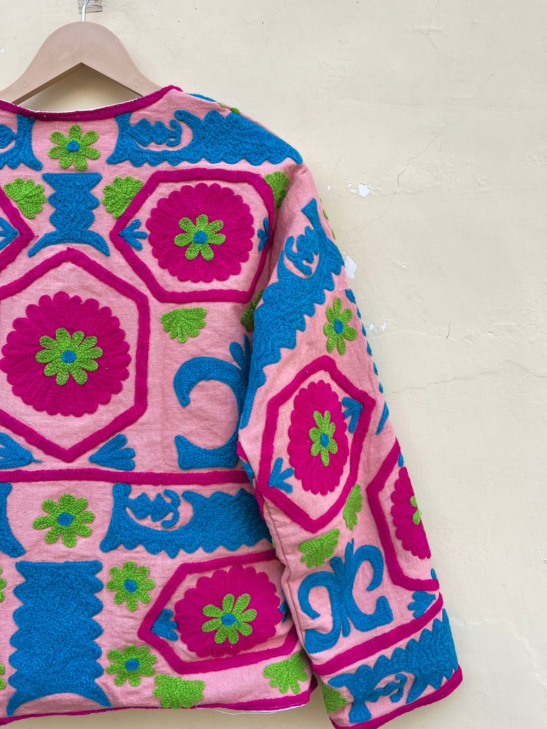 Puede incluir: Una chaqueta rosa con coloridos patrones florales bordados en tonos azules, verdes y rosas.