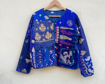 May include: A blue quilted jacket with a patchwork design featuring colorful embroidery and floral patterns. The jacket has a button closure and pockets.