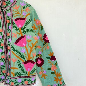 May include: A light green jacket with embroidered floral designs in shades of pink, orange, and purple. The jacket has a mandarin collar and a zipper closure.
