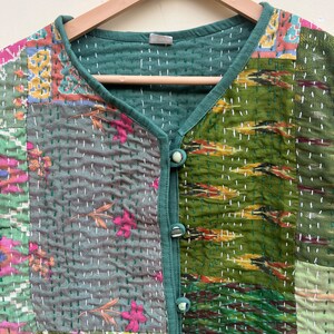 Puede incluir: Un chaleco acolchado verde con un dise&ntilde;o de patchwork que presenta varios patrones florales y geom&eacute;tricos. El chaleco tiene cuello en V y cierre de bot&oacute;n.