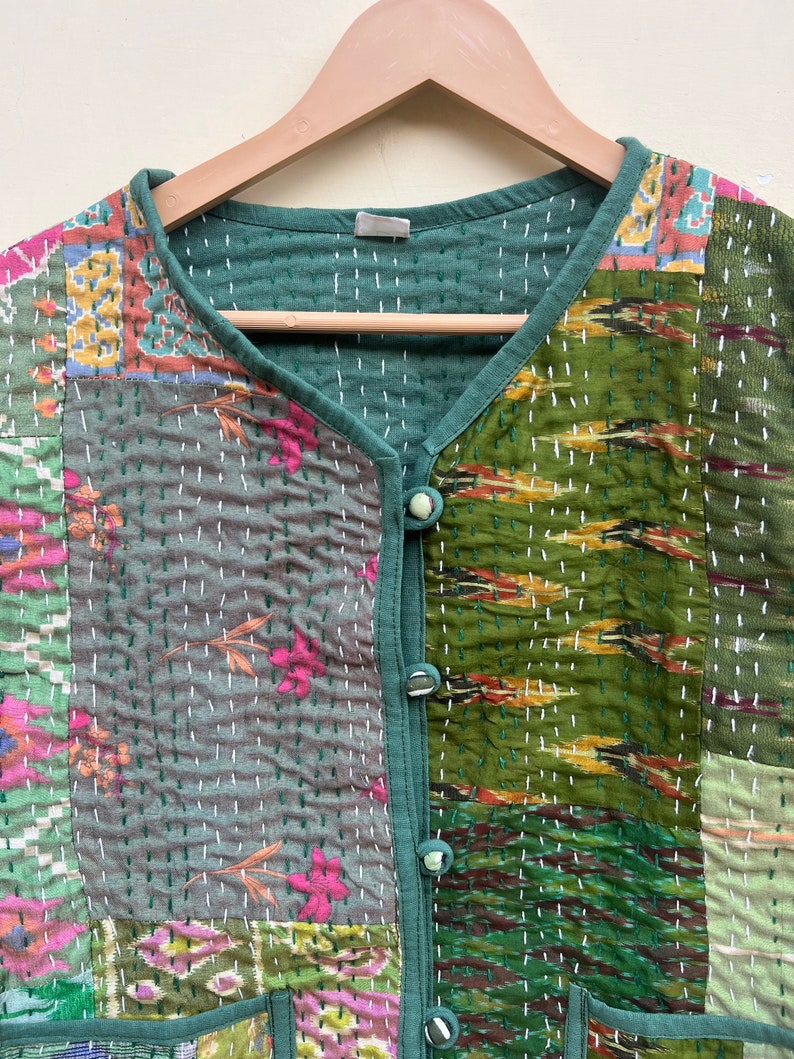 Puede incluir: Un chaleco acolchado verde con un dise&ntilde;o de patchwork que presenta varios patrones florales y geom&eacute;tricos. El chaleco tiene cuello en V y cierre de bot&oacute;n.
