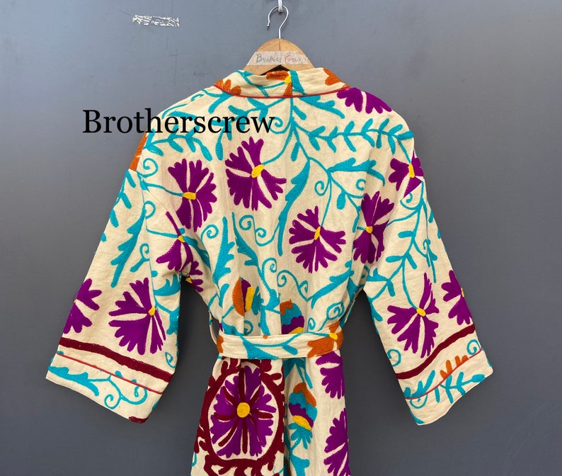 May include: A white robe with a floral pattern in shades of purple, turquoise, and orange. The robe has a tie belt and long sleeves.