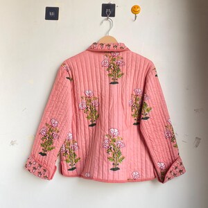 Pu&ograve; includere: Giacca rosa trapuntata con motivo floreale. La giacca presenta un collo, maniche lunghe e chiusura con bottoni. Il design floreale include fiori rosa e bianchi con foglie verdi.