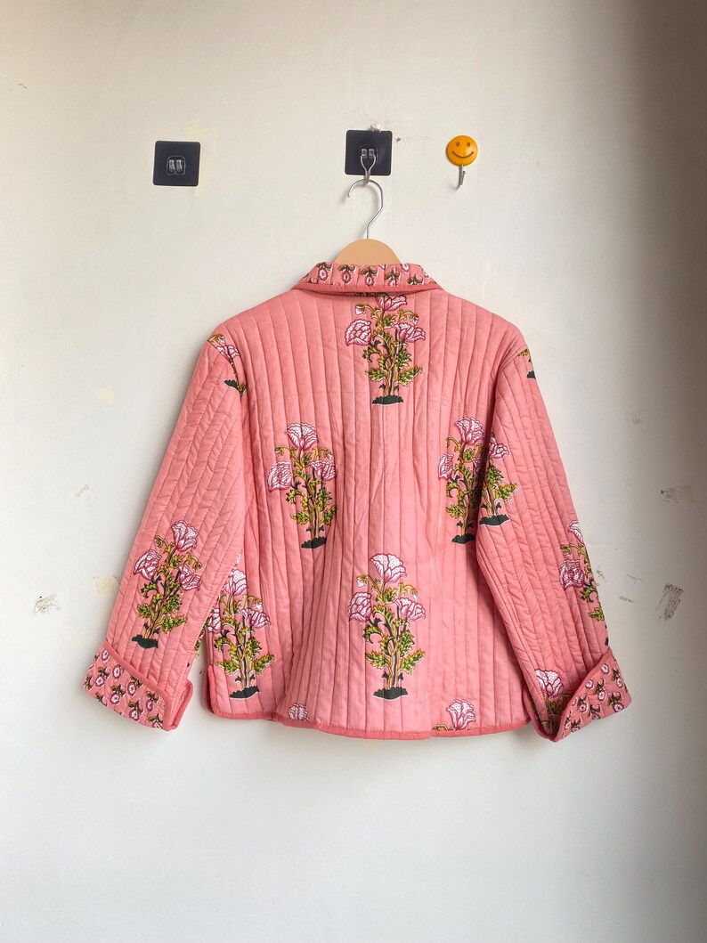 Pu&ograve; includere: Giacca rosa trapuntata con motivo floreale. La giacca presenta un collo, maniche lunghe e chiusura con bottoni. Il design floreale include fiori rosa e bianchi con foglie verdi.