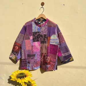 May include: A purple, pink, and brown patchwork quilted jacket with a mandarin collar and button closure. The jacket has a unique, vintage style and is made of a soft, comfortable fabric.