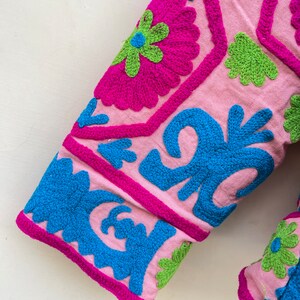 Puede incluir: Tela rosa con coloridos patrones bordados florales y geom&eacute;tricos en tonos rosa, azul y verde.