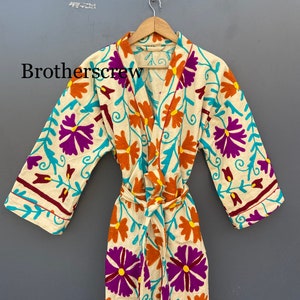 May include: A white robe with a floral pattern in shades of purple, orange, and turquoise. The robe has a tie belt and long sleeves.