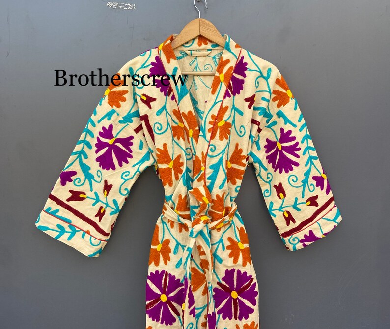 May include: A white robe with a floral pattern in shades of purple, orange, and turquoise. The robe has a tie belt and long sleeves.