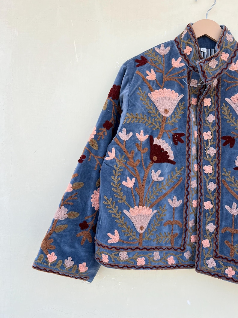 May include: A blue velvet jacket with floral embroidery in shades of pink, brown, and red. The jacket has a mandarin collar and a button closure.