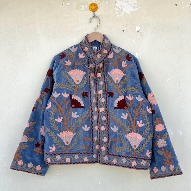 May include: A blue velvet jacket with floral embroidery in shades of pink, red, and green. The jacket has a stand-up collar and a button closure.
