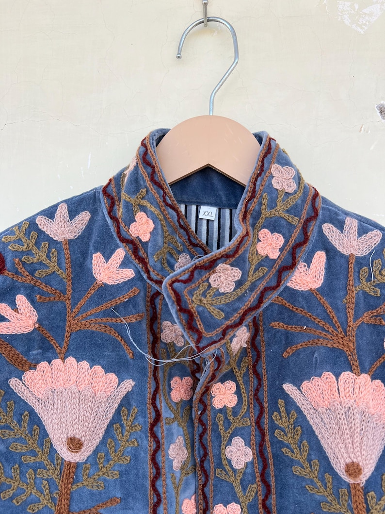 May include: A blue velvet jacket with embroidered floral details in shades of pink, brown, and green. The jacket has a collar and a button closure. The size tag reads "XXL".
