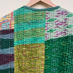 Puede incluir: Una colcha de retazos con una variedad de telas verdes, azules y marrones. La colcha est&aacute; hecha de cuadrados y rect&aacute;ngulos, y las costuras son visibles. La colcha est&aacute; colgada de una percha.