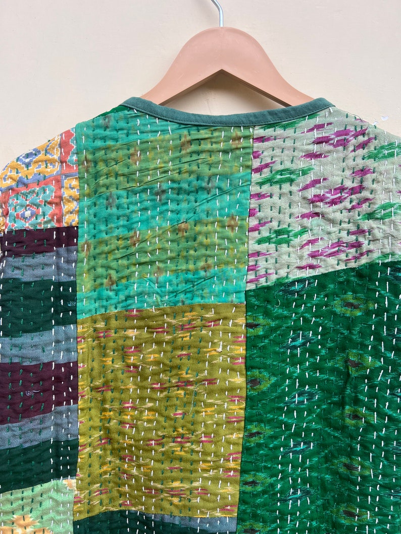 Puede incluir: Una colcha de retazos con una variedad de telas verdes, azules y marrones. La colcha est&aacute; hecha de cuadrados y rect&aacute;ngulos, y las costuras son visibles. La colcha est&aacute; colgada de una percha.
