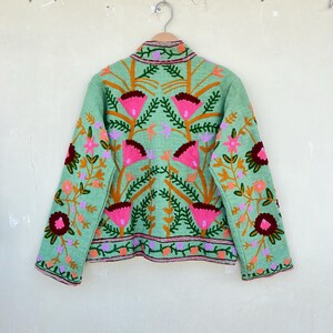 May include: A mint green jacket with a floral embroidery design. The embroidery features pink, orange, and burgundy flowers with green leaves.