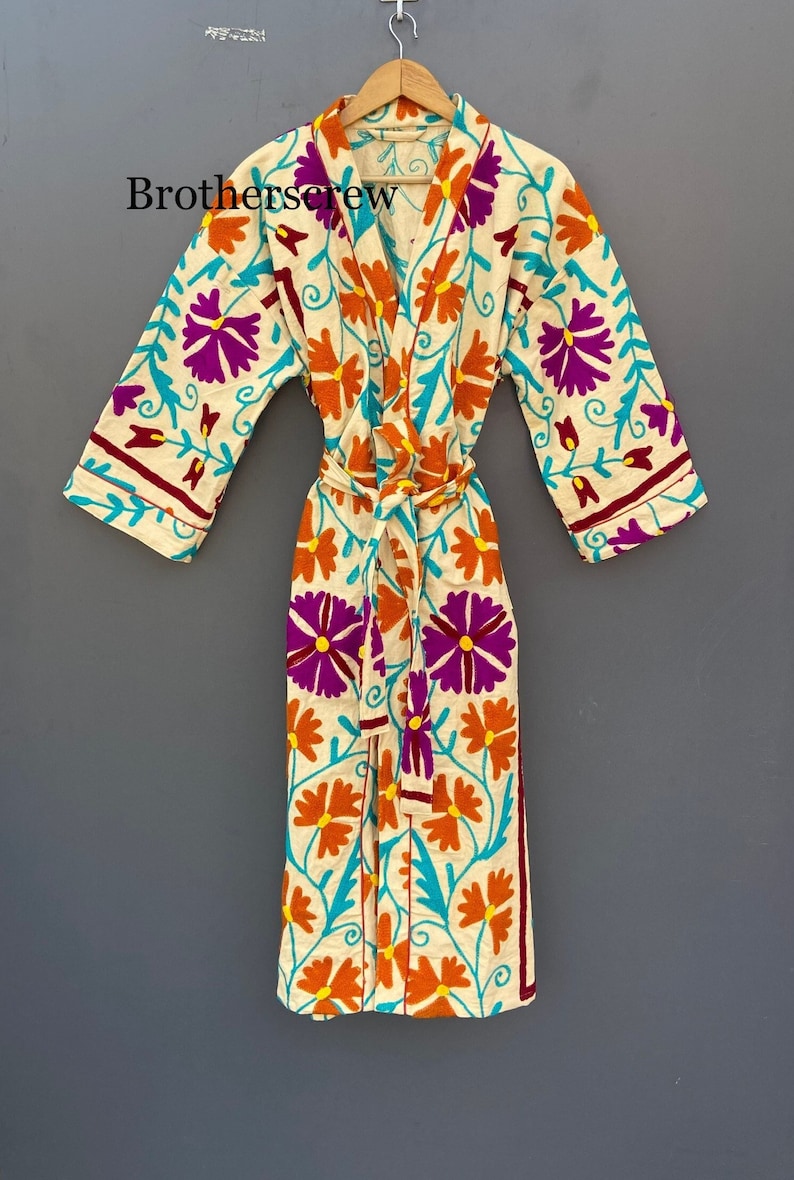 May include: A white cotton robe with a floral pattern in shades of orange, purple, and turquoise. The robe has a tie belt and long sleeves.