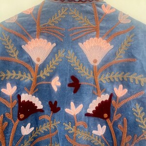 May include: A blue velvet jacket with intricate embroidery of flowers and leaves in shades of pink, brown, and burgundy.