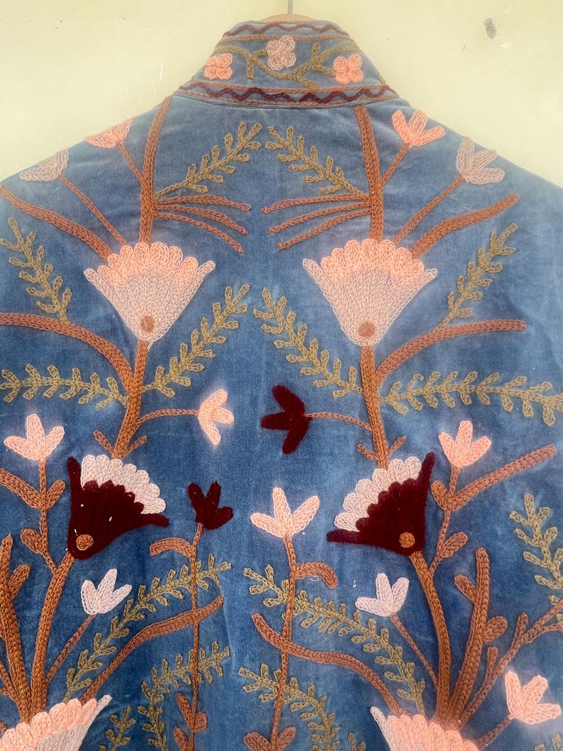 May include: A blue velvet jacket with intricate embroidery of flowers and leaves in shades of pink, brown, and burgundy.