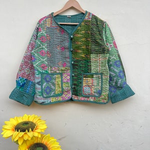 Puede incluir: Una chaqueta acolchada verde con un dise&ntilde;o de patchwork que presenta varios tonos de verde, rosa y azul. La chaqueta tiene un cierre de bot&oacute;n y dos bolsillos.