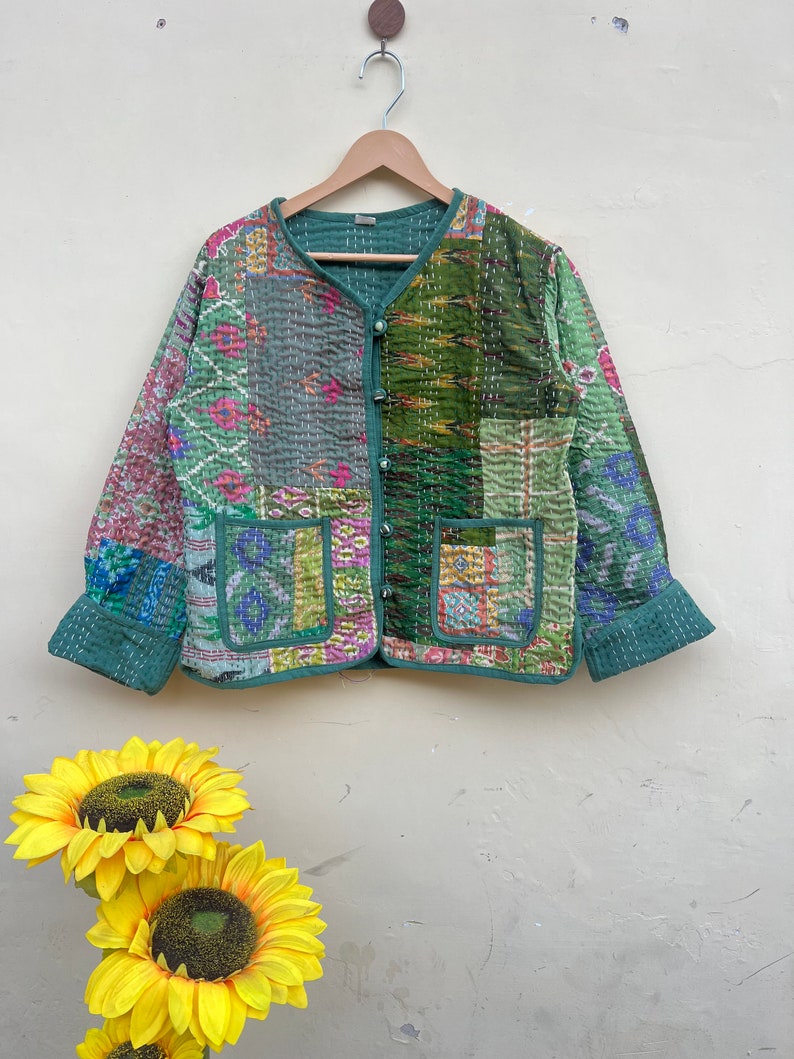 Puede incluir: Una chaqueta acolchada verde con un dise&ntilde;o de patchwork que presenta varios tonos de verde, rosa y azul. La chaqueta tiene un cierre de bot&oacute;n y dos bolsillos.