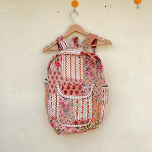 Puede incluir: Una mochila de estilo patchwork con estampado floral en tonos rosa, rojo, marrón y blanco. La mochila tiene un bolsillo grande en la parte delantera.