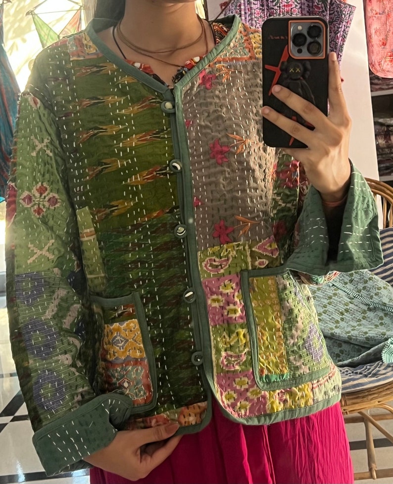 Puede incluir: Una chaqueta acolchada verde con un dise&ntilde;o de patchwork. La chaqueta tiene cierre de bot&oacute;n y dos bolsillos. La tela es una mezcla de diferentes patrones y colores, incluyendo verde, marr&oacute;n, rosa y amarillo.