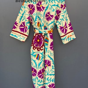 May include: A white robe with a floral pattern in shades of purple, blue, yellow, and orange. The robe has a tie belt and long sleeves.
