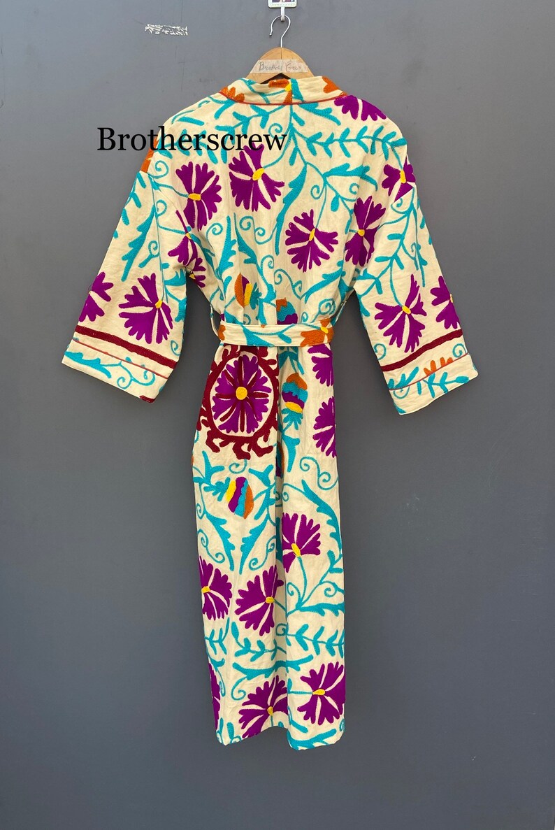 May include: A white robe with a floral pattern in shades of purple, blue, yellow, and orange. The robe has a tie belt and long sleeves.
