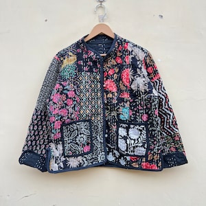 Puede incluir: Una chaqueta acolchada negra con un diseño de patchwork floral. La chaqueta tiene un cuello mandarín, mangas largas y dos bolsillos de parche.